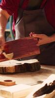 Vertikale Zimmermann im Versammlung Geschäft beginnend Wiederherstellung Projekt auf Holz Block, bewirbt sich Lack auf Oberfläche. Holzbearbeitung Spezialist Färbung Holz Planke mit Pinsel, tun Handarbeit im Studio, Kamera ein video