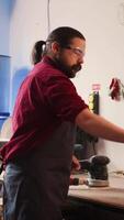 Vertical Carpenter holding power tool used to smooth surfaces by abrasion with sandpaper, changing cut off discs. Man preparing necessary equipment for furniture assembling job in studio, camera B video