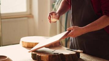 Holzbearbeitung Spezialist bewirbt sich Lack auf Holz zu bauen oben schützend Schicht. Schreiner im Versammlung Geschäft Lackieren hölzern Tafel nach Schleifen Oberfläche zu dafür sorgen Glätte, schließen oben Schuss, Kamera ein video