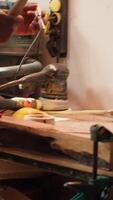 Vertical African american sculptor shaping raw timber using chisel and hammer in carpentry shop, creating wood art, wearing safety glasses. Artist making wood sculptures, engraving lumber with tools, camera A video