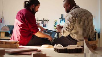 African american artist and colleague comparing wood art schematic with CAD software 3D render on laptop. Carpenters at work crosscheck drawing on clipboard with notebook blueprint, camera B video