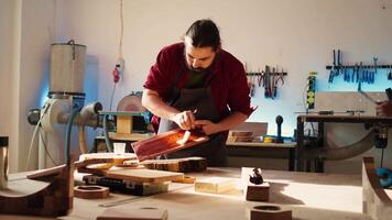 Carpenter in assembly shop starting restoration project on lumber block, applying lacquer on surface. Woodworking specialist coloring wood plank with paintbrush, doing handwork in studio, camera B video