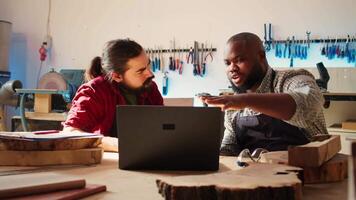 Woodworkers using CAD software on laptop to design wooden objects, pointing towards screen. Carpenters using program on notebook to help them do furniture assembling in joinery, camera B video