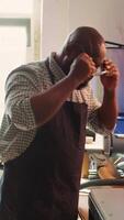 Vertical African american man in woodworking shop inspecting lumber piece before assembling furniture, checking for scratches. Cabinetmaker evaluates timber block, ensuring it meets quality standards, camera B video