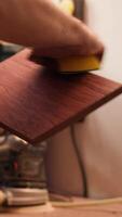 Vertical Carpenter doing last touches on piece of wood before using it for furniture assembly, sanding it with sandpaper. Woodworking expert doing woodworking process on lumber block, fixing damages, camera A video