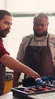 Vertical Master in carpentry shop instructing BIPOC worker to wear protection gear before assembling furniture. Cabinetmaker making sure apprentice uses safety earmuffs and glasses before starting work, camera B video