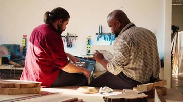 bipoc ambachtelijk en leerling vergelijken hout kunst stuk schematisch met cad software 3d geven Aan laptop. houtbewerking experts in studio kruiscontrole tekening Aan klembord met notitieboekje blauwdruk, camera b video