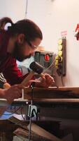 Vertical Man carving intricate designs into wood using chisel and hammer in carpentry shop, enjoying diy hobby. Woodworking specialist in studio shaping wooden pieces with tools, making wood art, camera B video