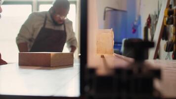 Man putting lumber block through spindle moulder, creating smooth edges on wooden piece. Joiner using heavy machinery to craft joints for furniture and structures, camera B close up video