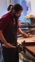 Vertical Woodworker using bench vise to hold lumber block, carving intricate designs into wood using chisel and hammer. Craftsperson using vice tool to clamp piece of wood, shaping log with tools, camera B video