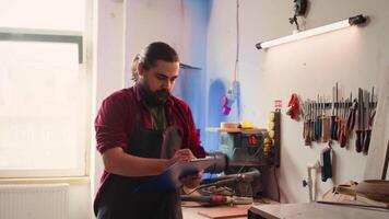 Woodworker looking over blueprints on laptop, brainstorming with colleague next steps in wood processing. Manufacturer and BIPOC apprentice reading furniture assembly schematics in studio, camera B video