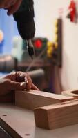 Vertical Woodworker using power drill to create holes for dowels in wooden board, close up. Carpenter sinks screws into wooden surfaces with electric tool, doing precise drilling for seamless joinery, camera B video