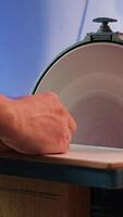 Vertical Woodworker shaping wooden bowl on disc sander in carpentry shop, showcasing precision. Cabinetmaker working in joinery, guiding wood against grinding machine rotating disc, camera A close up video