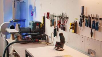 Chisels, screwdrivers, wrench and pliers on wall in furniture assembly shop next to electric router on workbench. Close up of woodworking gear on rack in joinery and power tool video