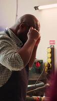 Vertical African american man in woodworking shop inspecting lumber piece before assembling furniture, checking for scratches. Cabinetmaker evaluates timber block, ensuring it meets quality standards, camera A video