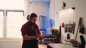 Craftsperson and colleague look over technical schematics to make commissioned wooden object. Manufacturer and coworker analyze blueprints to execute furniture assembling woodworking project, camera B video