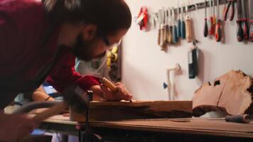 artesano utilizando banco tornillo a sostener madera bloquear, tallado intrincado diseños dentro madera utilizando cincel y martillo. artista usos vicio herramienta a abrazadera pedazo de madera, formación Iniciar sesión con herramientas, cámara si cerca arriba Disparo video