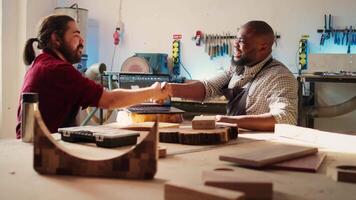 ébéniste tremblement collègue main après finition en utilisant cad Logiciel sur portable à conception en bois objets. charpentiers féliciter chaque autre pour emploi bien terminé dans meubles assemblage boutique, caméra b video