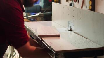 Woodworking expert wears protection gear, inserting plank in spindle moulder next to coworker. CNC machinist uses safety glasses while cutting lumber with wood shaper helped by colleague, camera A video