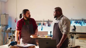 Carpenter and african american coworker verifying finished wood art product before sending it to client. Artisan and apprentice inspecting wooden object to correspond to requirements video