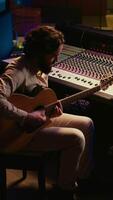 verticale talentuoso artista fare vivere prestazione con il suo chitarra nel professionale studio, registrazione nuovo canzoni con il suo Audio esperto. suono ingegnere miscelazione e mastering brani per lui. telecamera b. video