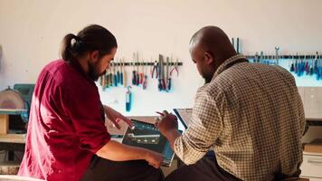 bipoc ambachtelijk en leerling vergelijken hout kunst stuk schematisch met cad software 3d geven Aan laptop. houtbewerking experts in studio kruiscontrole tekening Aan klembord met notitieboekje blauwdruk, camera een video