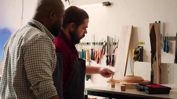 Schreiner Lehren Lehrling zu bohren Loch in Bauholz Block im Studio. Holzbearbeitung Schüler Lernen von Meister im Tischlerei Wie zu einfügen Nagel in Stück von Holz mit Leistung bohren, Kamera ein video