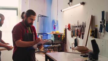 artesão desenhando plantas em bloco de anotações dentro estúdio com bipoc colega de trabalho dentro fundo resolução tarefas. fabricante olhando às técnico esquemas para executar marcenaria projetos, Câmera b video