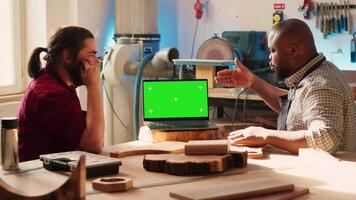 Woodworker looking over blueprints on green screen laptop in CAD software with apprentice. Craftsperson and coworker designing custom 3D furniture on chroma key notebook in studio, camera A video