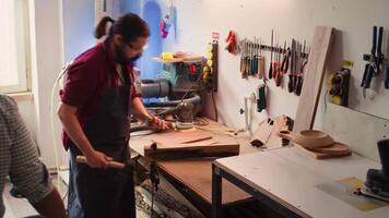 Woodworker using bench vise to hold lumber block, carving intricate designs into wood using chisel and hammer. Craftsperson using vice tool to clamp piece of wood, shaping log with tools, camera B video