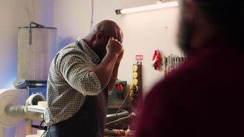 African american man in woodworking shop inspecting lumber piece before assembling furniture, checking for scratches. Cabinetmaker evaluates timber block, ensuring it meets quality standards, camera A video