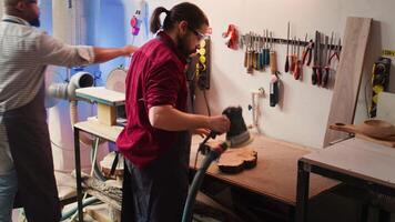 Craftsperson works with orbital sander with sandpaper on lumber to achieve smooth finish, checking quality. Woodworking expert in carpentry shop using angle grinder to fix wooden surface, camera B video