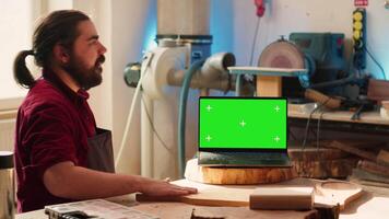 Upbeat men using CAD software on isolated screen laptop, debating wood design to use. Smiling cabinetmakers chatting, using program on chroma key notebook to make furniture schematics, camera A video