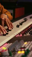 Vertical African american producer uses control desk with automatic equalizer, mixer and sliders to edit tracks in post production. Sound engineer processing audio recordings, mixing console. Camera B. video