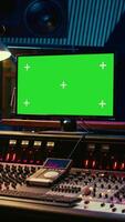 Vertical Sound designer editing and recording tracks with mixing console in control room, twisting knobs and pressing key buttons. Audio engineer producing music with greenscreen on monitor. Camera B. video