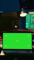 Vertical Audio technician leveling sound on recorder mixing console, having a laptop that shows greenscreen display. Producer turns up the volume of tracks in professional studio, control room. Camera B. video