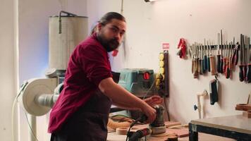 Artisan uses safety goggles to prevent workplace accidents while removing imperfections on wood. Man wearing protective equipment to avoid injury while using angle grinder to sander plank, camera A video