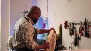 Carpenter in woodworking shop spinning wood block around, inspecting it before assembling furniture. BIPOC cabinetmaker in joinery studio evaluating lumber block, checking for damages, camera A video