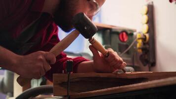 Artisan using bench vise to hold timber block, carving intricate designs into wood using chisel and hammer. Artist uses vice tool to clamp piece of wood, shaping log with tools, camera A close up shot video