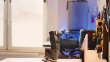 Close up of electric router on spindle moulder in furniture assembly shop with woodworking tools on rack in background. Focus on hand powered equipment used for sanding wood in studio, panning shot video