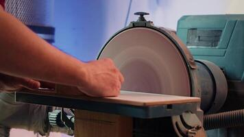 Woodworker shaping wooden bowl on disc sander in carpentry shop, showcasing precision. Cabinetmaker working in joinery, guiding wood against grinding machine rotating disc, camera A close up video