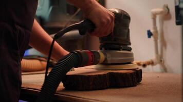 Cabinetmaker at workbench using orbital sander with fine sandpaper on lumber to achieve smooth finish. Woodworking specialist uses angle grinder on wood for professional results, close up, camera A video