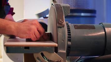 Artisan sanding wooden object on disc sander in assembling shop. Diy hobby enjoyer working in joinery, guiding wood against grinding machine rotating disc to create art, camera A close up shot video