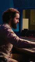 Vertical Portrait of audio technician adjusting volume levels on recordings by using pre amp knobs and fader on control room board. Music producer working on mix and master techniques. Camera B. video