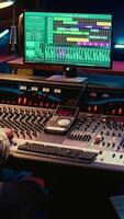 Vertical Audio technician mixes individual tunes to create balanced sound after recording session in professional studio. Sound engineer editing tracks with mixing console and production software. Camera A. video