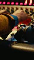 vertical africano americano sonido ingeniero utilizando auriculares a escucha a audio grabaciones en enviar producción, ajustando volumen niveles con edición software interfaz. experto en estudio controlar habitación. cámara una. video