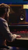 Vertical Audio technician mixes individual tunes to create balanced sound after recording session in professional studio. Sound engineer editing tracks with mixing console and production software. Camera A. video