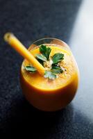 Mango Carrot Apple Smoothie in a glass on dark background with glass straw photo