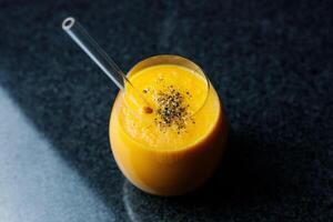 Mango Carrot Apple Smoothie in a glass on dark background with glass straw photo