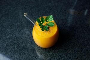 Mango Carrot Apple Smoothie in a glass on dark background with glass straw photo